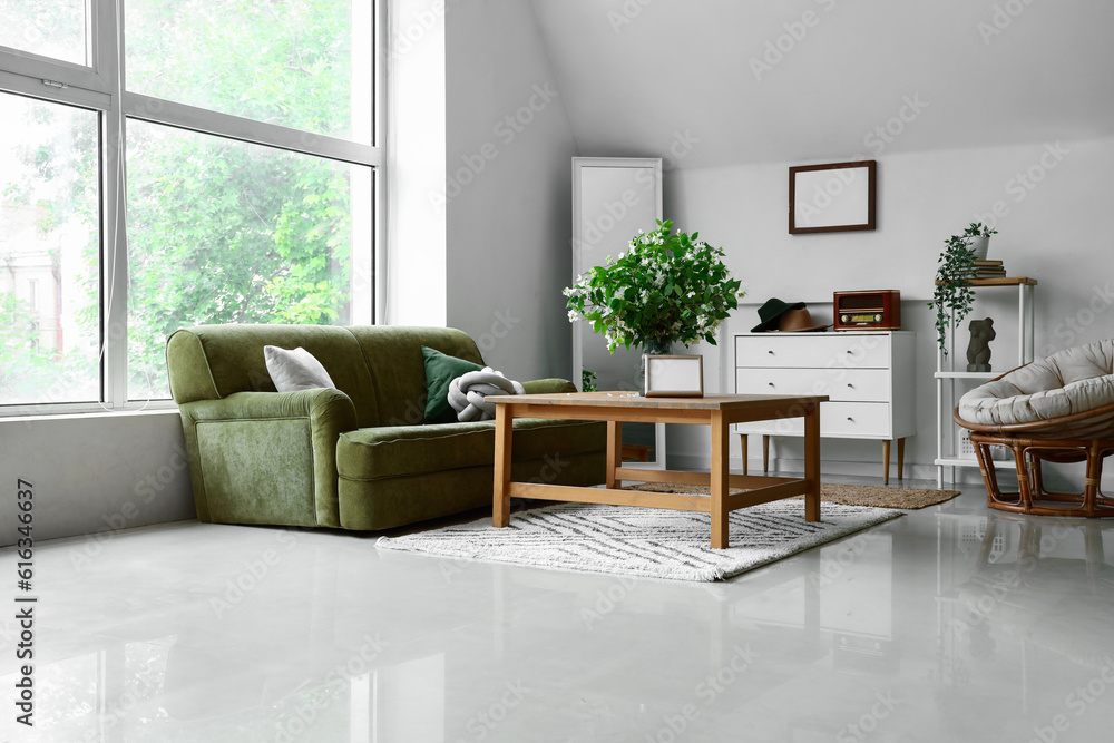 Fototapeta premium Interior of light living room with green sofa and blooming jasmine flowers on coffee table