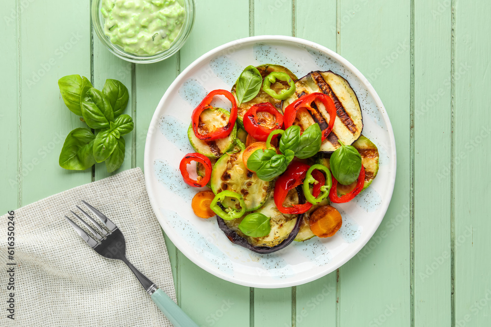 Plate with grilled vegetables and basil on green wooden table Plate with grilled vegetables and basil on green wooden table