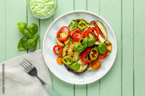 Plate with grilled vegetables and basil on green wooden table