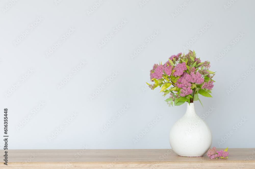 pink spirea in white vase on wooden shelf pink spirea in white vase on wooden shelf