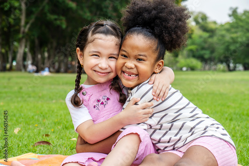 Two African American cheerful little girl sitting on the mat and hugging each other with love in the garden