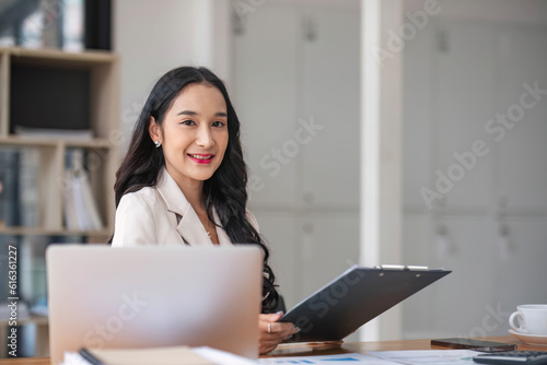 A beautiful and professional Asian businesswoman using her laptop to manage his tasks, working at the office.