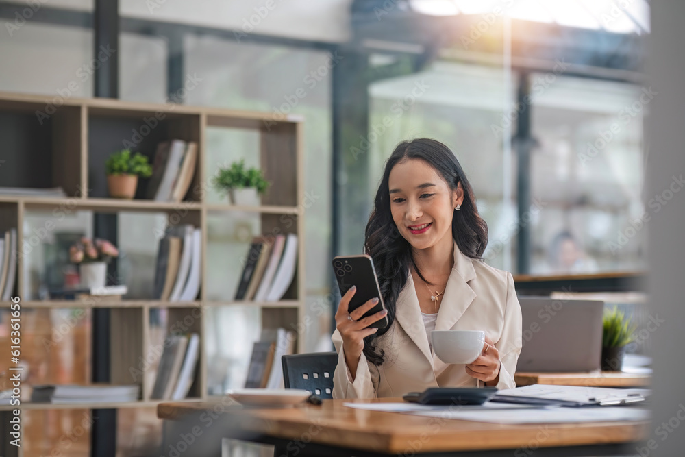 A beautiful and professional Asian businesswoman reviewing a business report and sipping her morning coffee at her desk in the office. A beautiful and professional Asian businesswoman reviewing a business report and sipping her morning coffee at her desk in the office.