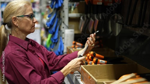 Attractive happy mature woman looking at small pruning knife for trimming branches in garden tool area of a large hardware store.