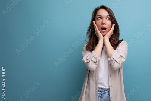 surprised puzzled 30s dark haired woman in shirt and jeans on blue background