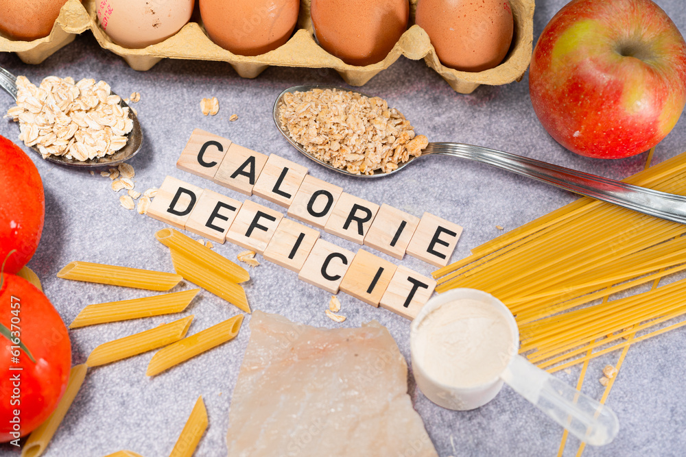 the inscription calorie deficit next to healthy food products. Flat lay photo showing weight loss and getting in shape - obrazy, fototapety, plakaty 