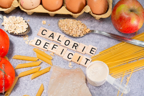the inscription calorie deficit next to healthy food products. Flat lay photo showing weight loss and getting in shape
