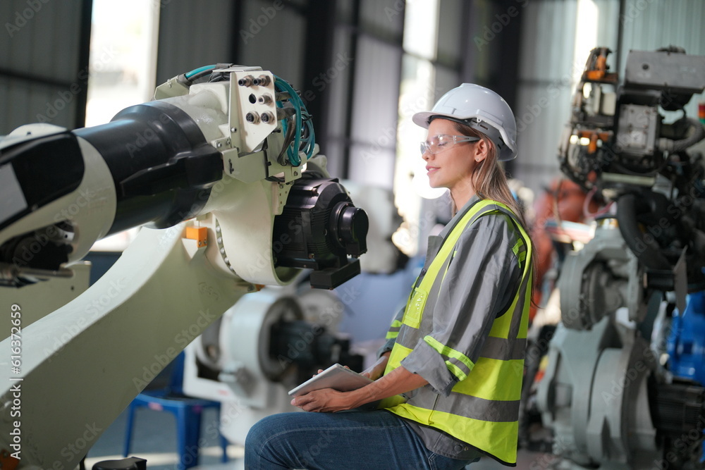 Robotic Arm engineer check on equipment in its with software of an Artificial Intelligence, Programming development technology work. Female industrial engineer working at automated robotic factory.. Robotic Arm engineer check on equipment in its with software of an Artificial Intelligence, Programming development technology work. Female industrial engineer working at automated robotic factory..