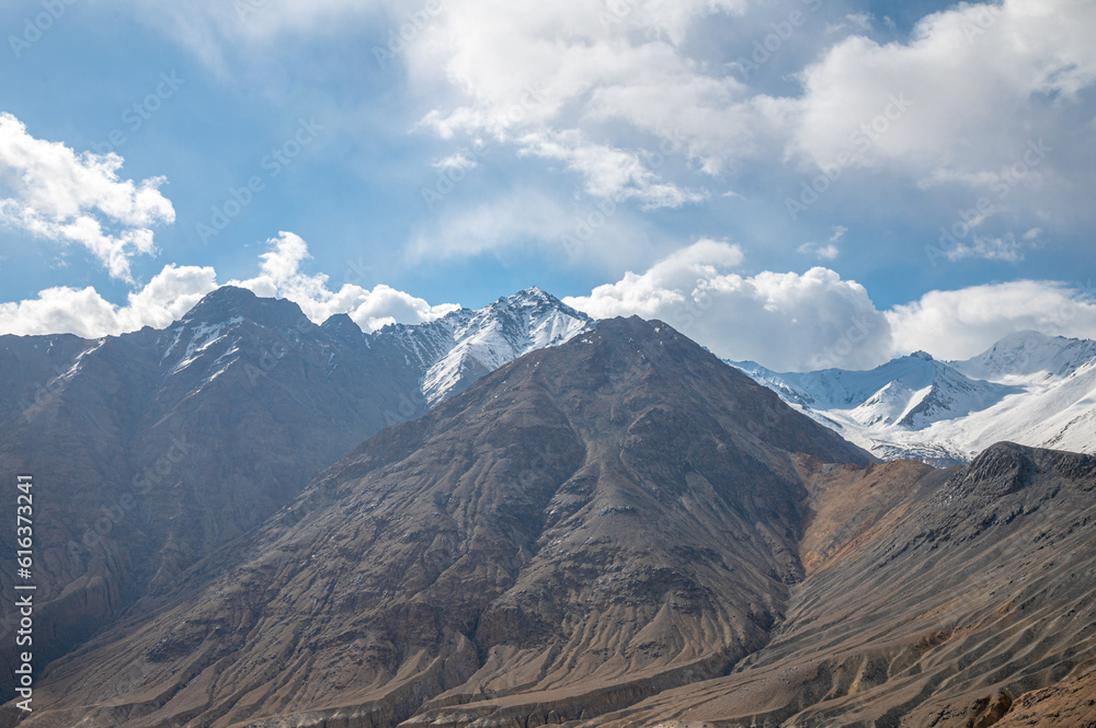 The barren landscape of Leh, Ladakh. Landscape view of rocky land surrounded by snow-covered Himalayas and Dramatic clouds.