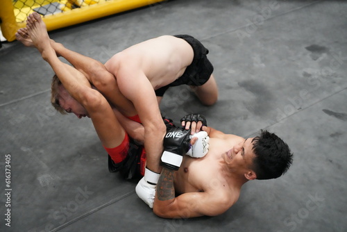 Intense Grapple: Two male athletes engage in a fierce grappling match, one applying a submission hold on the other in a combat sports arena.