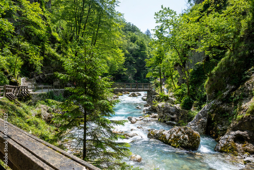 Tourists walking over wooden bridge, suspended over wonderful Soca river tributary, deep in the slovenian Alps
