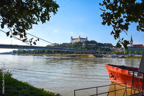 Photography A Red Boat by the Danube with Bratislava Castle in the Background