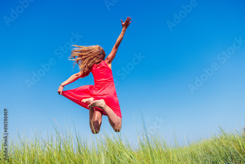 Happy woman in red dress jumping on blue sky and green grass- relaxing, active, fun,freedom,wellness concept