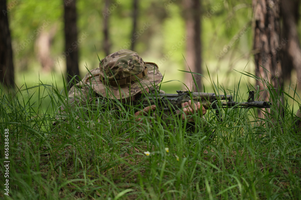 A soldier with a machine gun is lying in the grass, taking aim A soldier with a machine gun is lying in the grass, taking aim
