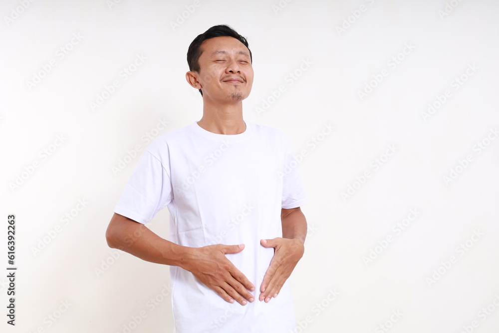 Asian funny man standing while holding his tummy. He feels full. Isolated on white background Asian funny man standing while holding his tummy. He feels full. Isolated on white background