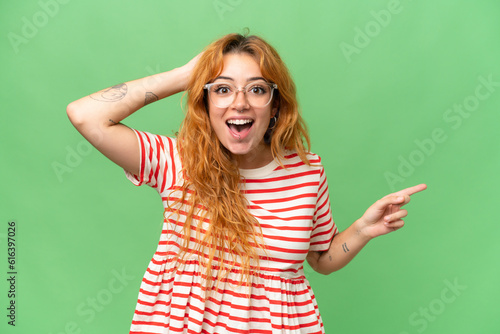Young caucasian woman isolated on green screen chroma key background surprised and pointing finger to the side