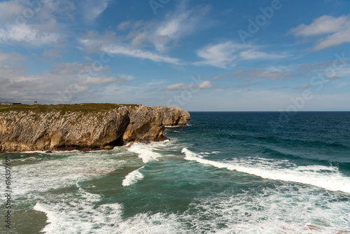 Panoramic view of the tourist beach of Guadamia on the coast of Asturias on its way out to sea with rough seas and some waves surrounded by cliffs on a sunny day.