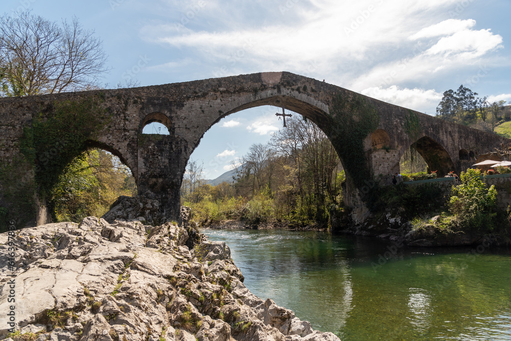 Panoramic view of the Roman bridge in the tourist town of Cangas de Onís in Asturias, built over the river Güeña, surrounded by vegetation and nature.