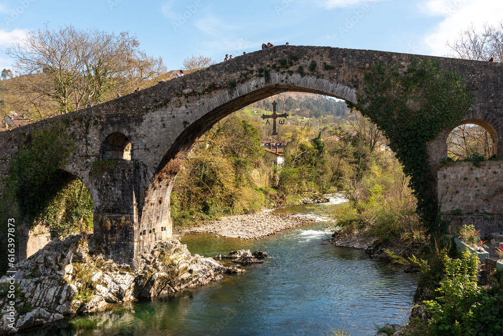  Impressive view of the Roman bridge in the tourist village of Cangas de Onís in Asturias, built over the river Güeña, surrounded by vegetation and nature during the sunset