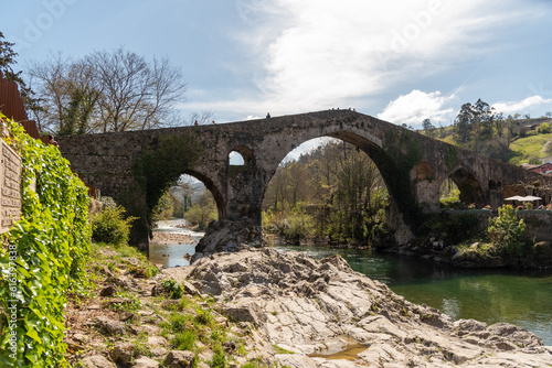 View of the Roman bridge in the tourist town of Cangas de Onís in Asturias, built over the river Güeña, surrounded by vegetation and nature at sunset.