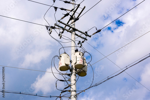 Concrete gray round electric pole with transverse brown metal diamond-shaped frames construction with clusters of insulators, to which main electrical high-voltage wires attached by means of tripwires