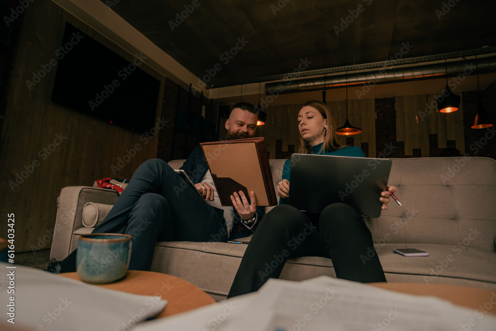 Handsome male business person looking at his female colleague lap top while she is looking at the documents he is holding Handsome male business person looking at his female colleague lap top while she is looking at the documents he is holding