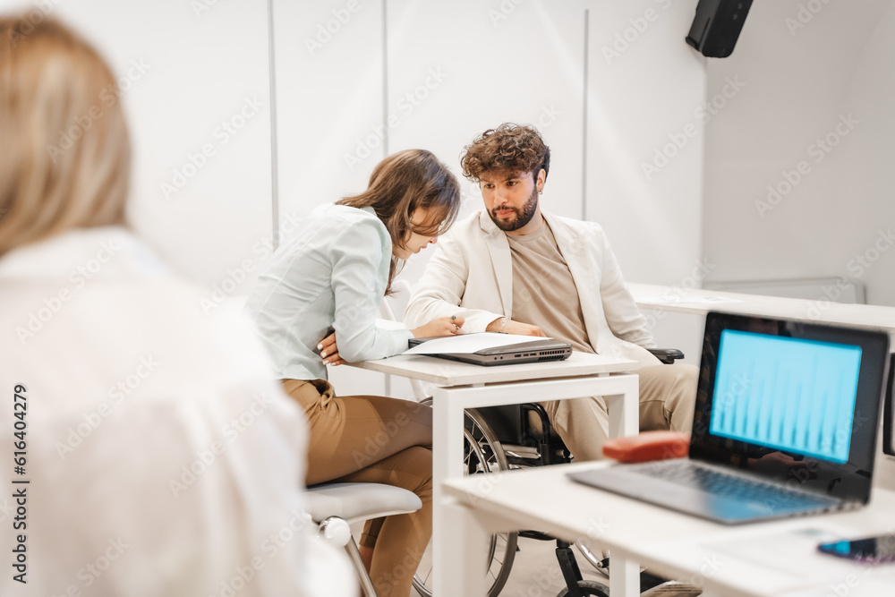 Handicapped male person looking at his gorgeous female colleague while she is reading from the document Handicapped male person looking at his gorgeous female colleague while she is reading from the document