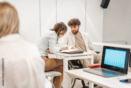 Handicapped male person looking at his gorgeous female colleague while she is reading from the document