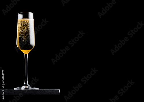 Elegant glass of yellow champagne with bubbles on black marble board on black background. Space for text