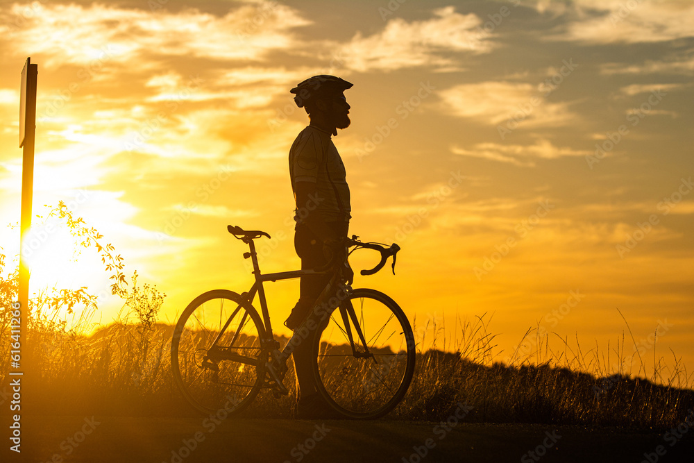 Fototapeta premium Sports and outdoor activities concept.Silhouette of cyclist riding a road bike on open road in evening during sunset.