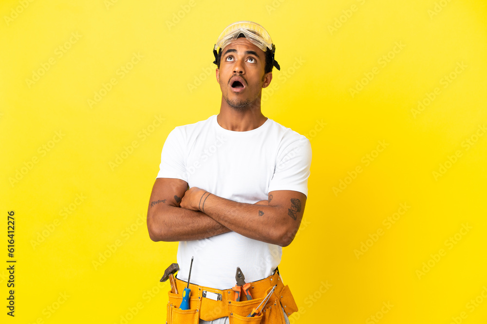 African American electrician man over isolated yellow wall looking up and with surprised expression