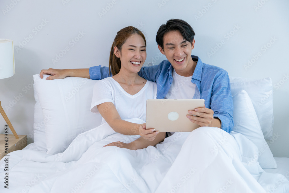 Young couple watching tv series laughing happily using tablet and sitting on sofa bed Young couple watching tv series laughing happily using tablet and sitting on sofa bed