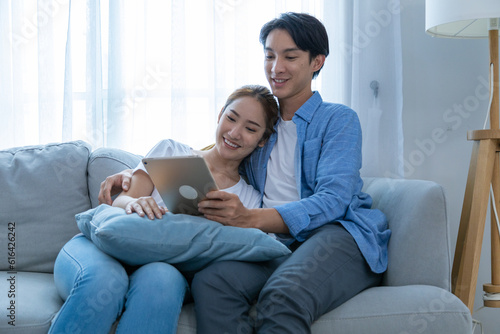 Young couple watching tv series laughing happily using tablet and sitting on sofa bed