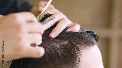 hairstylist creating trendy hairstyle for a young man using scissors and a comb