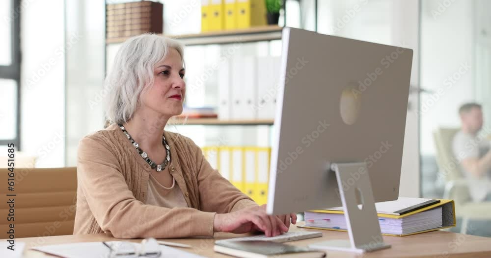 Mature business woman using laptop computer sitting at desk. Attentive senior elderly employee working in office Mature business woman using laptop computer sitting at desk. Attentive senior elderly employee working in office