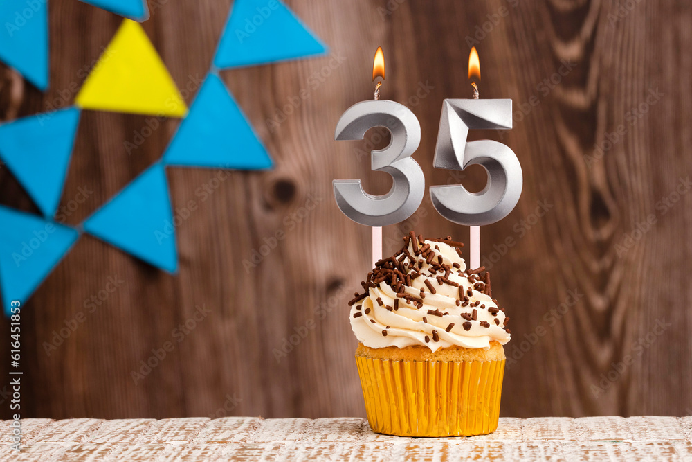 burning candle - birthday number 35 on wooden background with pennants