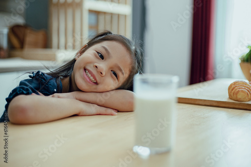 Portrait of Asian little girl looking a cup of milk in kitchen in house. Young preschool child girl or daughter stay home with smiling face.