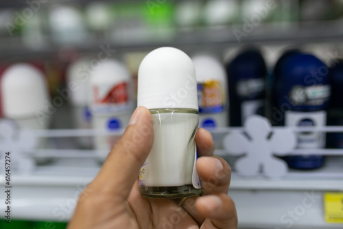 Hand holding deodorant bottle on shelf in supermarket blur background.