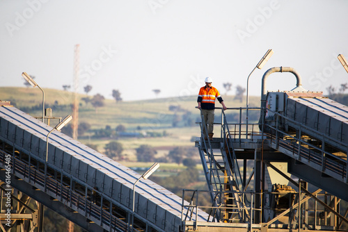 Worker wearing industrial safety vest with white helmet standing on a tall steel