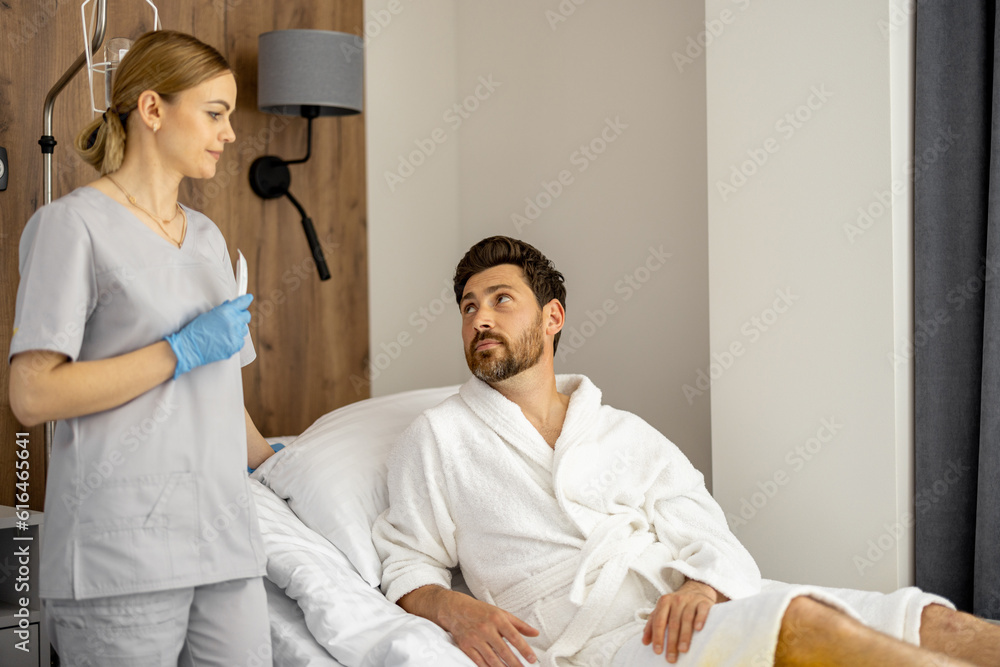 Obraz premium Nurse talks with adult male patient in mdeical ward. Medical support and assistance during the rehabilitation period after surgery