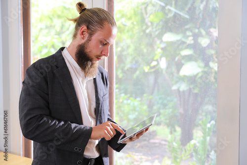 Bearded young businessman holding and working on tablet