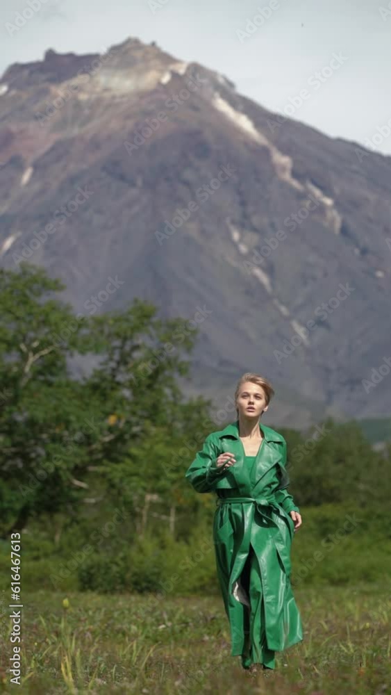 Fashionable woman model dressed in green long leather coat running in forest on background of mountain on summer weather. Vertical video, slow motion. Handheld shot front view. Part of video series Fashionable woman model dressed in green long leather coat running in forest on background of mountain on summer weather. Vertical video, slow motion. Handheld shot front view. Part of video series