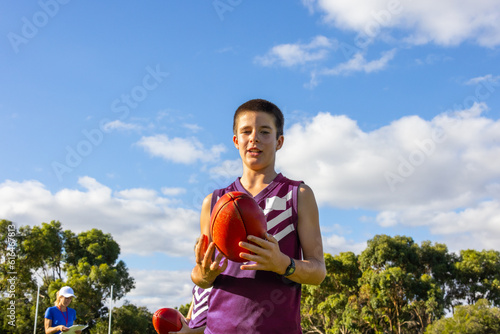 young boy in foreground holding Australian rules football with coach in background photo