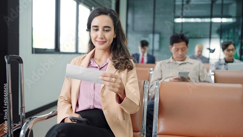 Young hispanic latin woman passenger checking depature boarding pass while sitting on chair in terminal departure gate waiting flight at international airport