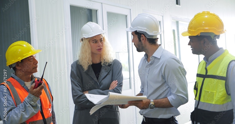 Team of industrial engineers in hard hats talking together working with project blueprint at industry manufacturing factory. Teamwork concept Team of industrial engineers in hard hats talking together working with project blueprint at industry manufacturing factory. Teamwork concept