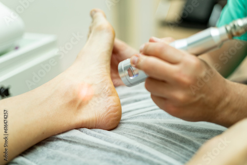 An unrecognizable podiatrist performs laser therapy on an athlete's foot. Laser therapy treatment, laser in podiatry. Foot care in medical centers. photo