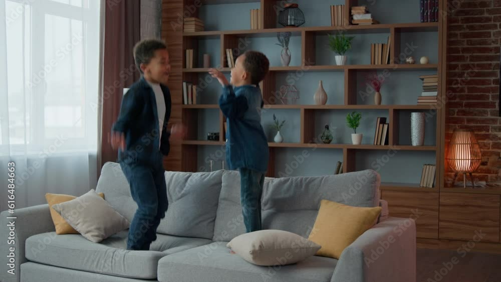 Two little boys children African American active siblings ethnic kids brothers jumping on soft sofa in cozy living room enjoy jump on couch at home playing game funny play having fun together indoors Two little boys children African American active siblings ethnic kids brothers jumping on soft sofa in cozy living room enjoy jump on couch at home playing game funny play having fun together indoors