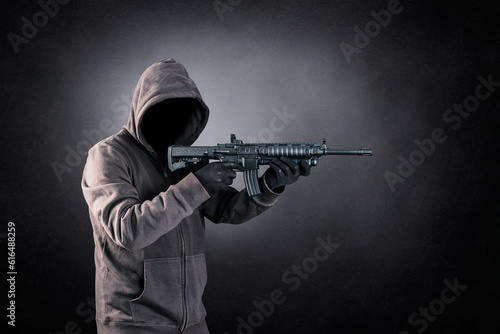 Hooded man with assault rifle over dark misty background