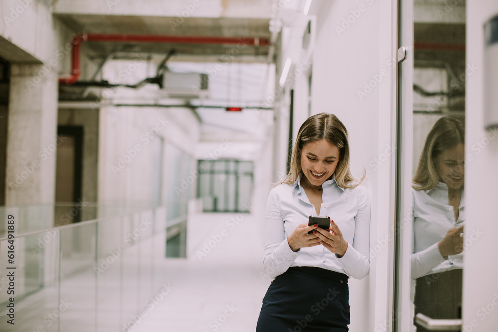 Young business woman using mobile phone in the office hallway Young business woman using mobile phone in the office hallway
