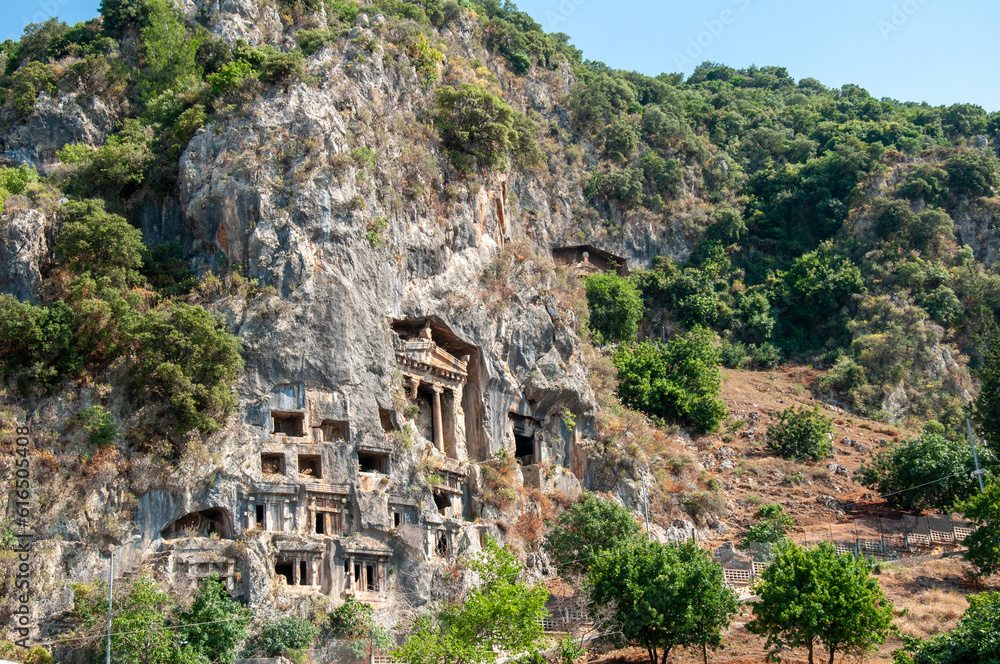 Amyntas rock tombs - 4th BC tombs carved in steep cliff. Tourist stands in front of the door. City of Fethiye, Turkey. Amyntas rock tombs - 4th BC tombs carved in steep cliff. Tourist stands in front of the door. City of Fethiye, Turkey.